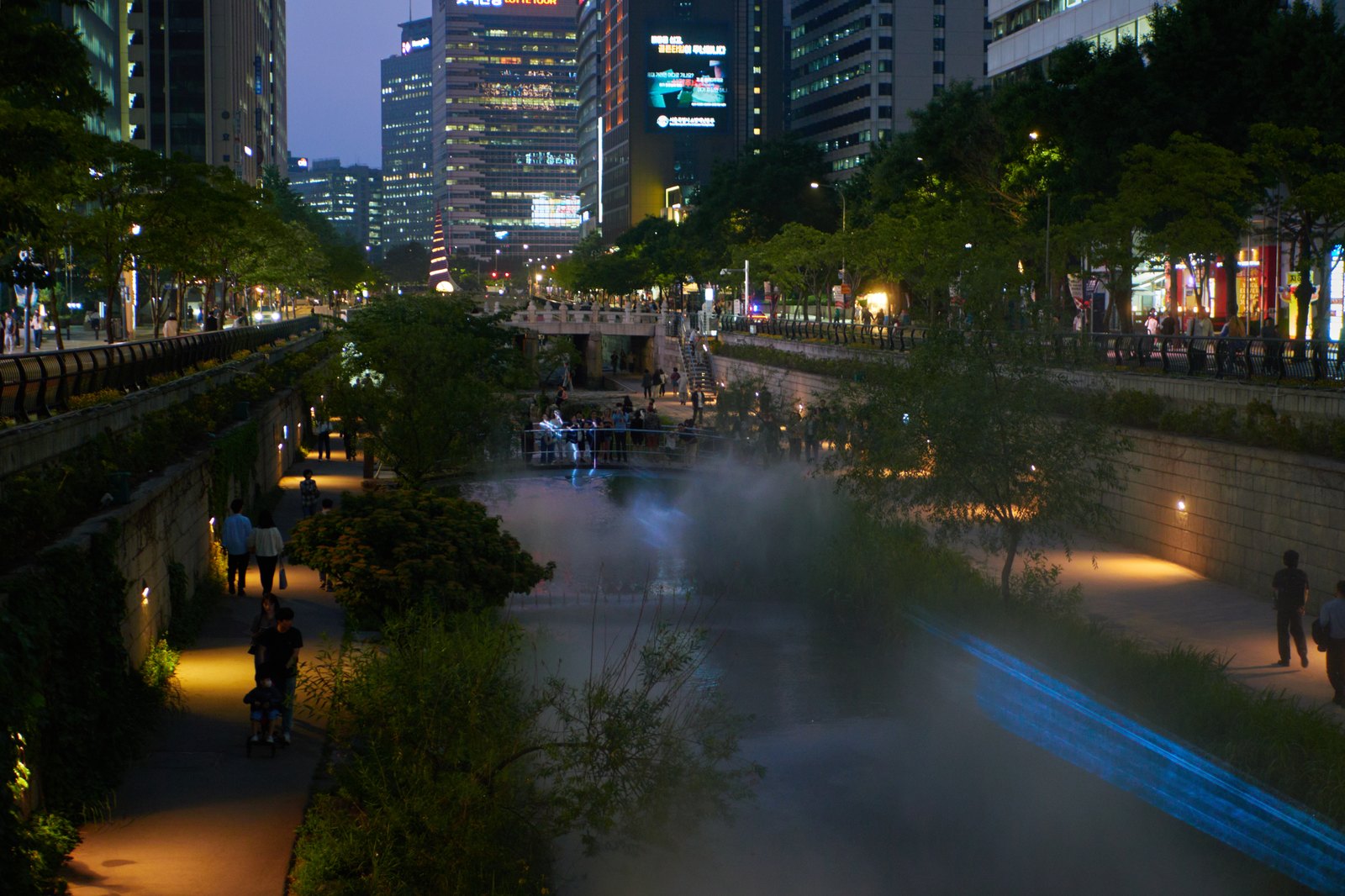 Cheonggyecheon stream at night with pedestrians walking the restored waterway below downtown Seoul's towers