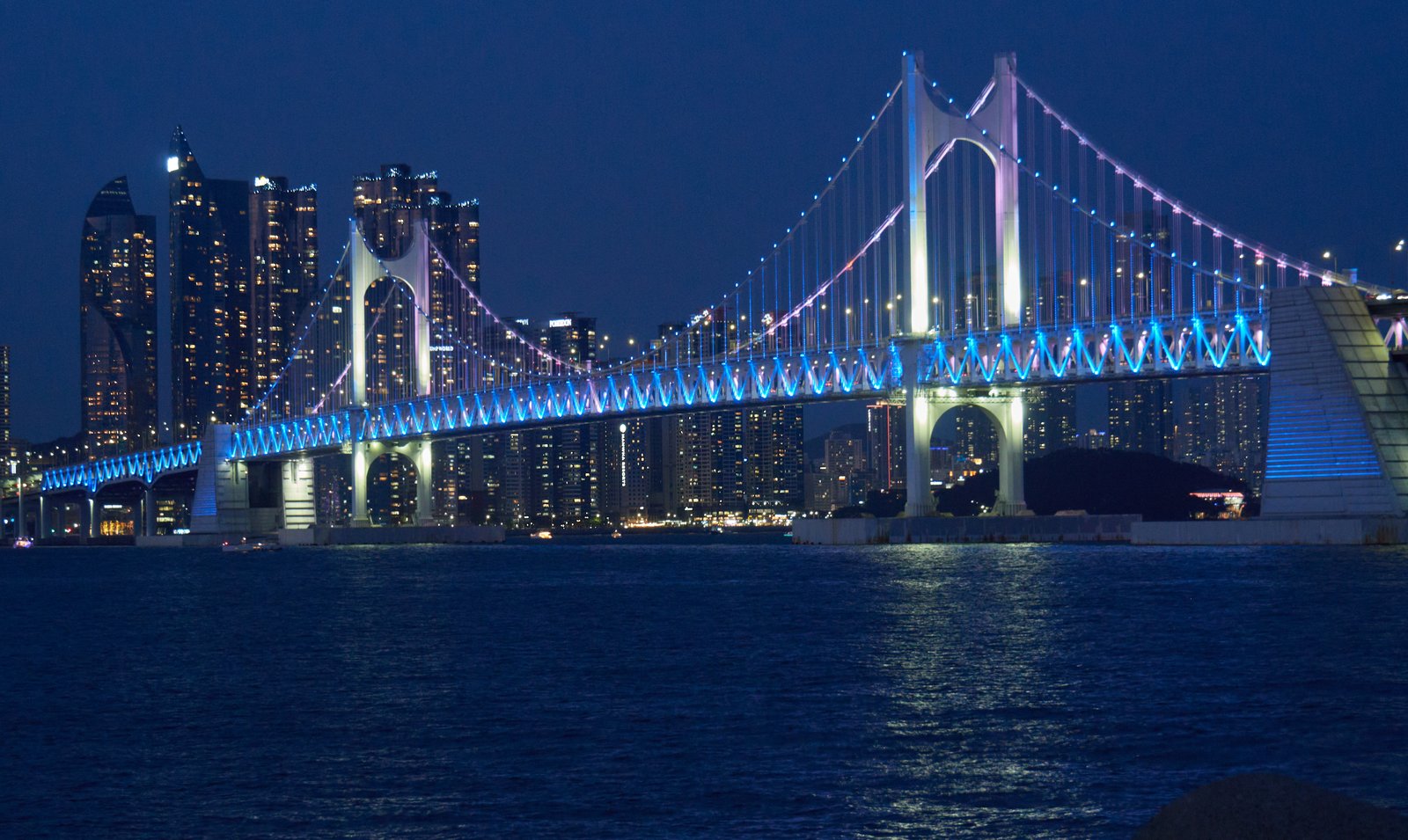 Gwangan Bridge illuminated in blue at night over the sea off Gwangalli Beach, Busan
