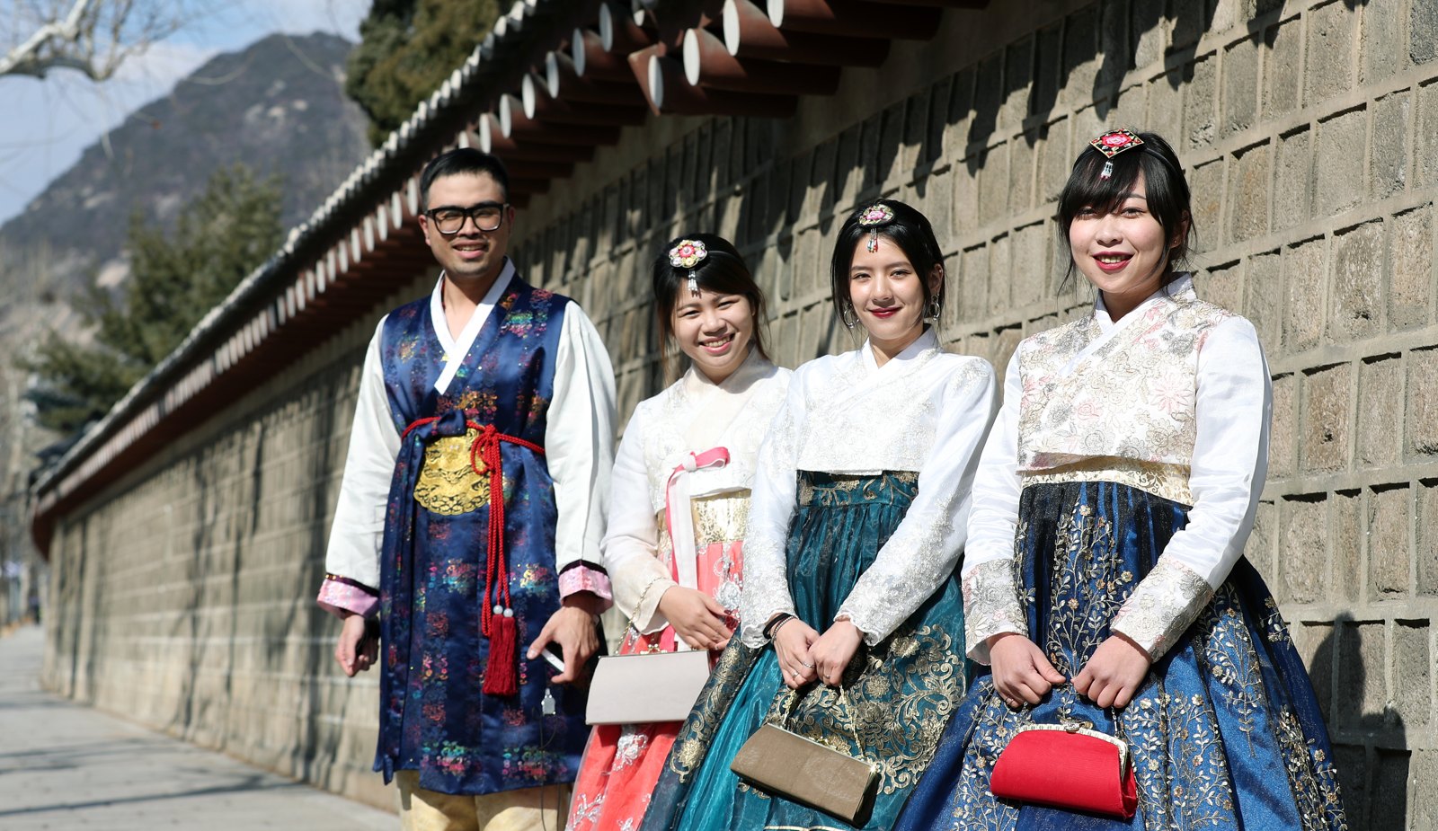Four visitors in hanbok walking along the stone wall beside Gyeongbokgung Palace in Seoul