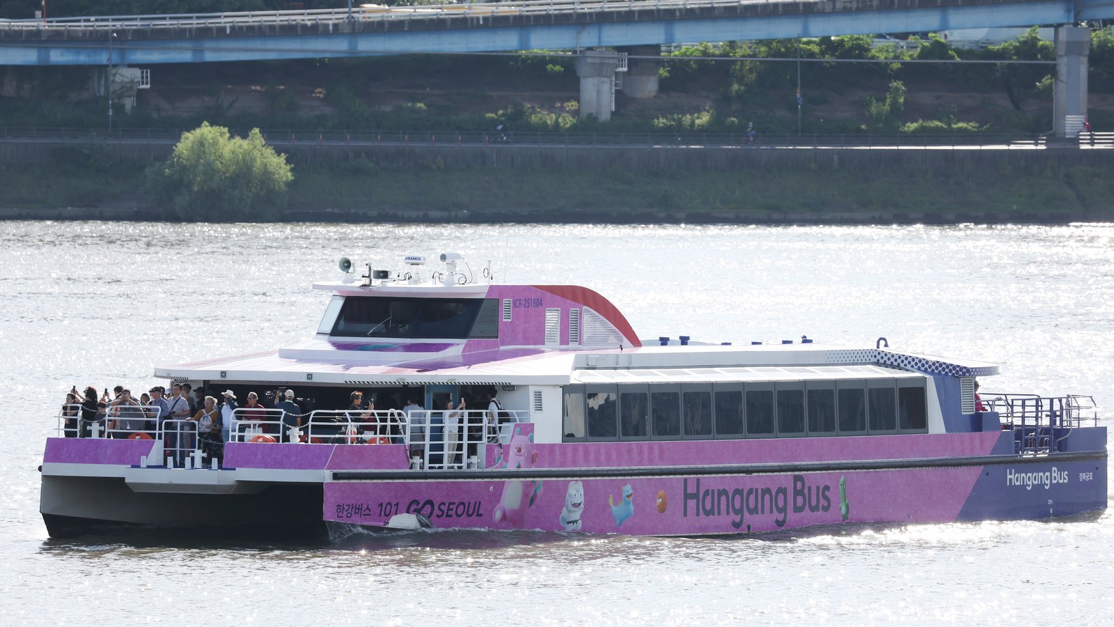 A pink-and-white Hangang Bus ferry with passengers on the open deck sailing on the Han River in Seoul, September 2025
