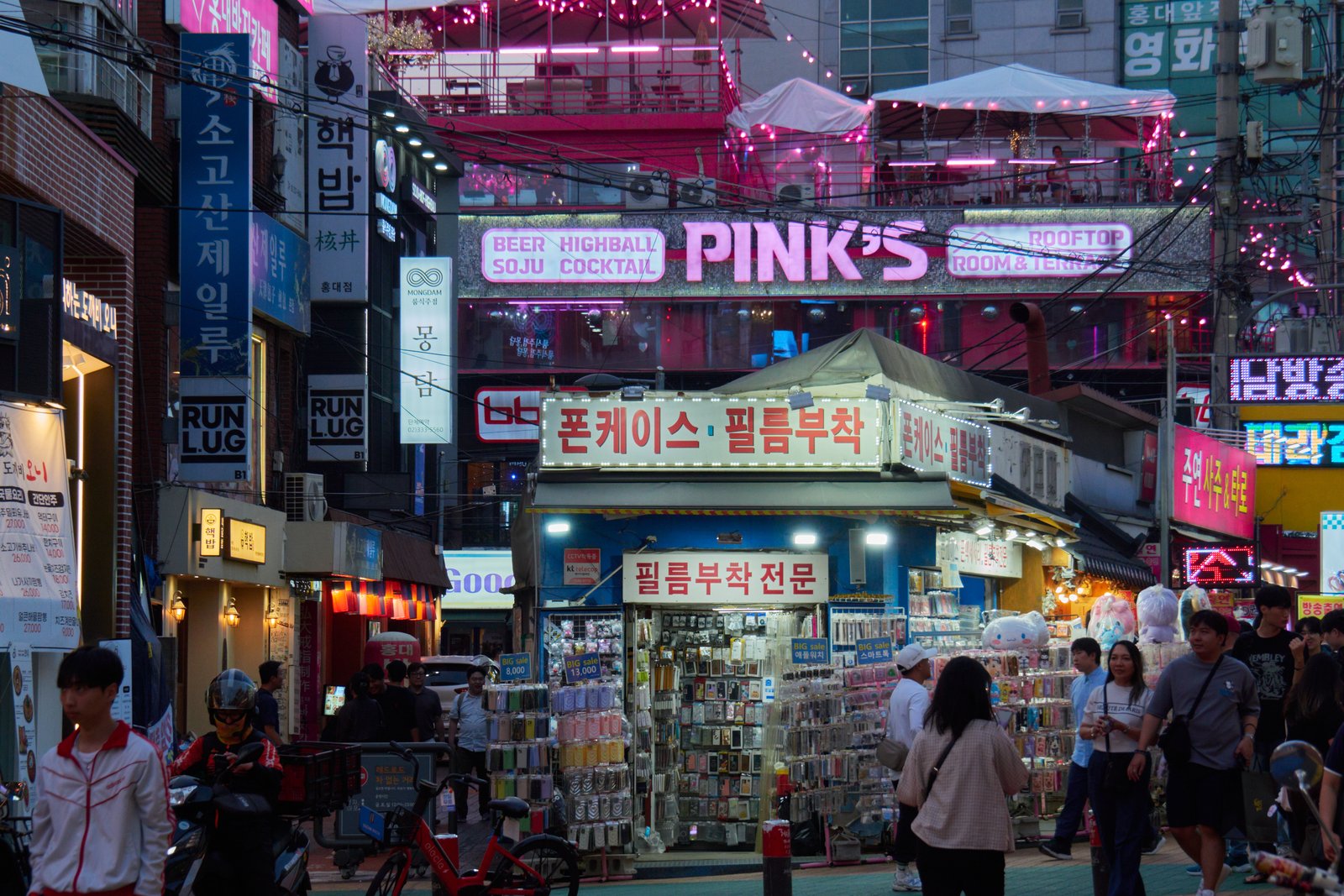 Crowded Hongdae shopping street lined with shops and signs in the evening, Seoul