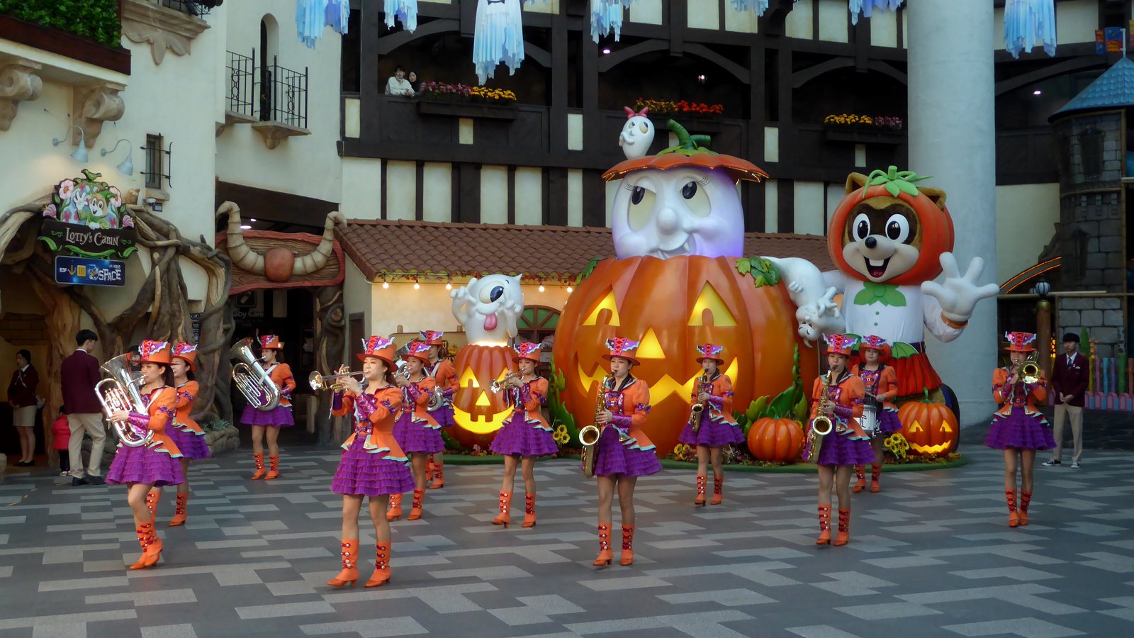 A brass band in orange and purple Halloween costumes performing in front of giant jack-o'-lantern figures inside Lotte World, Seoul (2019)