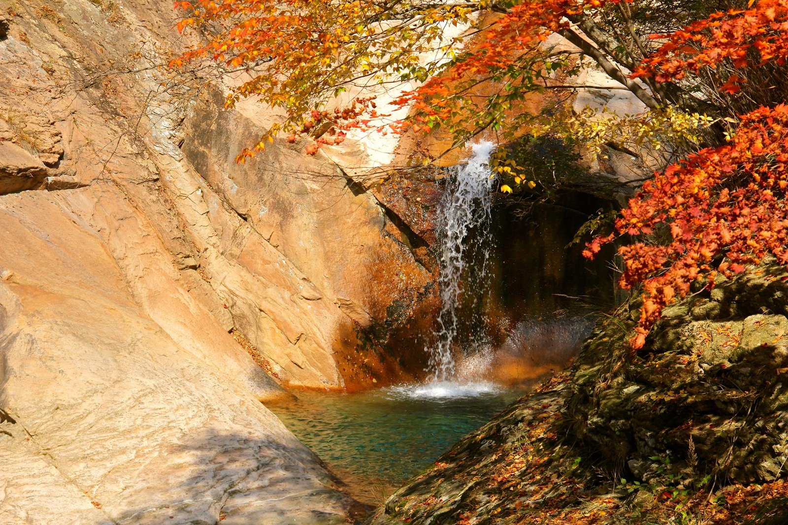 Waterfall and pool framed by red and orange autumn foliage in Seoraksan National Park